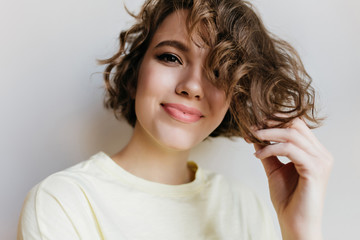 Wall Mural - Close-up portrait of happy young woman with trendy makeup playing with short hair. Indoor photo of enchanting curly girl isolated on white background.