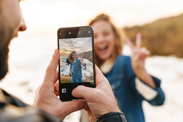 Wall Mural - image of young caucasian couple taking photo on cellphone by seaside