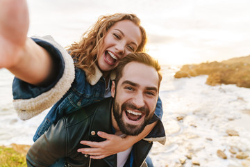 Wall Mural - image of beautiful young couple piggybacking while walking by seaside