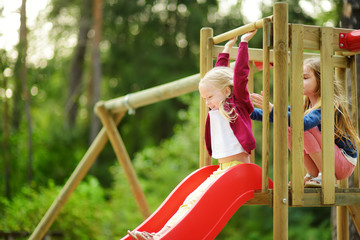 two cute little girls having fun on a playground outdoors on warm summer day