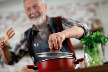 Wall Mural - Old man in kitchen. Senior man cooking delicious food. 