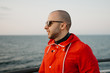 © Roman Tyukin - A man with stubble in a red jacket in the sunglasses aboard a ship looking at the sunset. Close portrait.