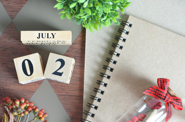 July 2. Date of September month. Number Cube with a flower, Rose bottle and notebook on Diamond wood table for the background.