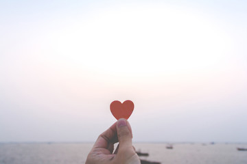 Close up of hand man holding a paper heart with the sea background. love concept, happy valentine.