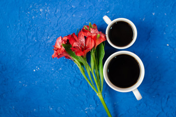 Top view with two cups of coffee with red flower on the copy space. Background for women's day on March 8. Blue table. A woman and a stylish workplace. March 8 and the concept of 