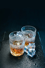 two expensive glasses of whiskey with ice on a black stone tray