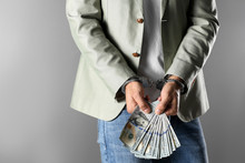 Man In Handcuffs Holding Bribe Money On Grey Background, Closeup