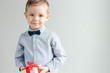 Cute boy holding a white gift box with red ribbon in his hands. Smiling baby with gift in hands.