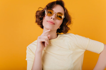 Sticker - Enchanting girl with short dark hair posing with interested face expression. Studio portrait of charming pale woman in orange sunglasses.