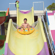 Happy smiling boy gliding down colorful water slide in water park during his summer holidays. He is making numerous splashes around.