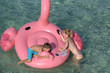 European woman and her son swimming in sea at resort on huge inflatable pink flamingo. They on summer vacations.