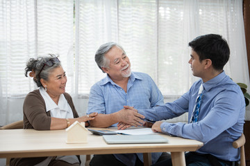 Smiling satisfied senior couple making sale purchase deal concluding contract hand get house key from real estate agent,happy older family and broker shake hands agreeing to buy new house at meeting.