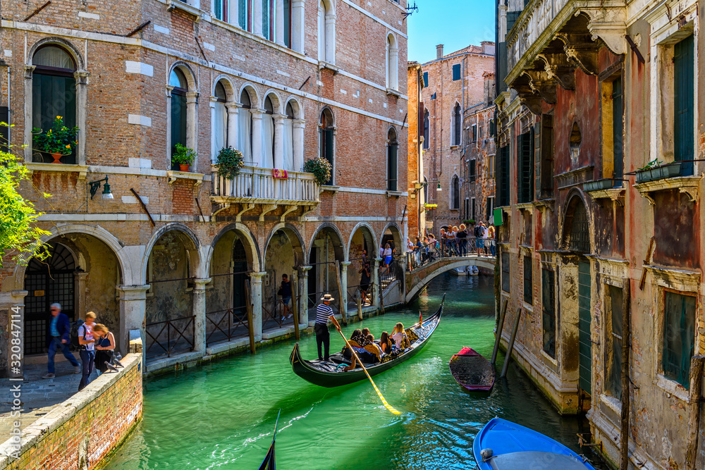 Narrow canal with gondola and bridge in Venice, Italy. Architecture and landmark of Venice. Cozy cityscape of Venice. - obrazy, fototapety, plakaty 