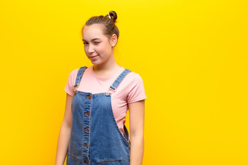 young blonde pretty girl looking happy and friendly, smiling and winking an eye at you with a positive attitude against yellow wall