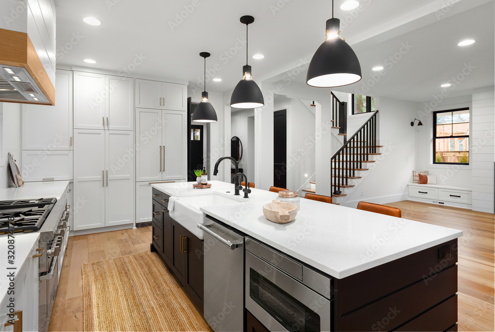 Beautiful white kitchen with dark accents in new modern farmhouse style luxury home. Features large island with farmhouse sink, dishwasher, microwave and view of living room and stairs. - obrazy, fototapety, plakaty 