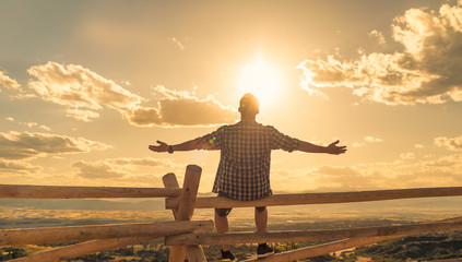 happy man sitting outdoors looking up to the sky with arms outstretched. people freedom and happines