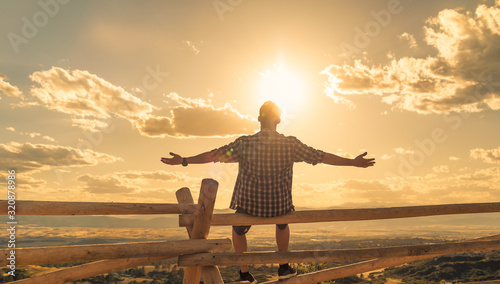 Happy man sitting outdoors looking up to the sky with arms outstretched Poster Mural XXL
