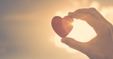 Hand holding up heart with rays of sunshine shinning through. 