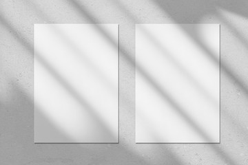 Two empty white vertical rectangle poster or business card mockups with diagonal window shadow on the gray concrete wall.Flat lay, top view. For advertising, brand design, stationery presentation.