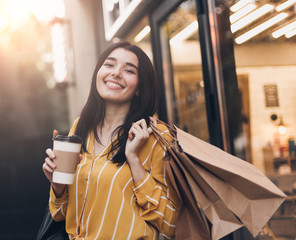 Young pretty woman in yellow skirt with shopping bags, cup of black coffee and smartphone