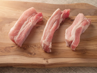 Three raw uncooked pork belly portions on a wooden cutting board. Selective focus.