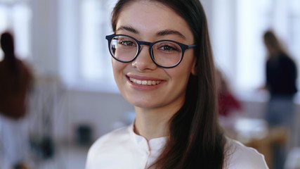 Wall Mural - Close-up portrait, happy young brunette design professional business woman in eyeglasses smiling at camera at office.