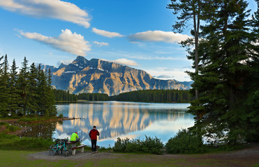 Overview of Two Jack Lake at sunset in Banff National Park with two bikers in the foreground. 