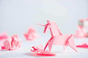 pink origami unicorn with crumpled paper balls. creative process is writing, light background
