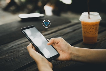 Wall Mural - Woman hand using smart phone with wifi icon abstract background at coffee shop with colorful bokeh light. Technology business and modern lifestyle concept.