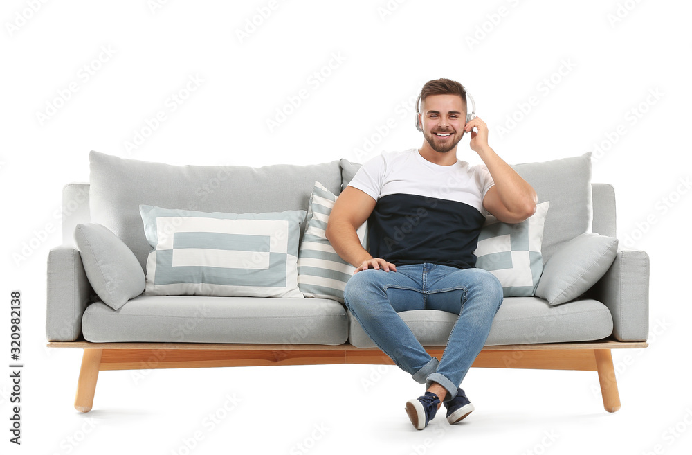 Young man listening to music while sitting on sofa against white background