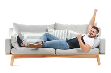 Canvas Print - Young man listening to music while lying on sofa against white background