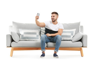 Canvas Print - Young man taking selfie while sitting on sofa against white background