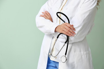 Young African-American doctor with stethoscope on color background