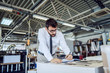 © Dusan Petkovic - Handsome caucasian bearded supervisor with eyeglasses and in shirt and tie checking on quality of printed sheets and writing down notes in notebook while standing in printing shop.