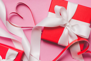 Red gift boxes tied with a white ribbon, two paper hearts on a pink background