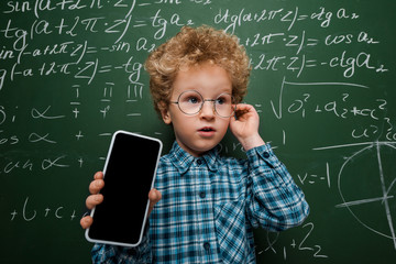 Wall Mural - smart kid in glasses holding smartphone with blank screen near chalkboard with mathematical formulas