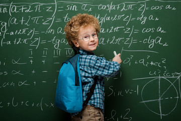 Wall Mural - happy kid in glasses writing mathematical formulas on chalkboard