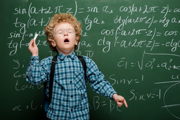 Wall Mural - curly kid in glasses sneezing near chalkboard with mathematical formulas