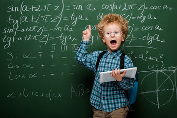 Wall Mural - smart kid in glasses having idea while holding digital tablet near chalkboard
