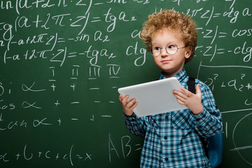Wall Mural - smart kid in glasses holding digital tablet near chalkboard with mathematical formulas