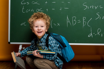 Wall Mural - happy kid laughing while holding books near chalkboard with mathematical formulas