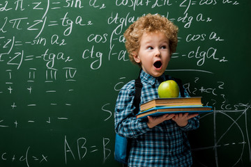 Wall Mural - surprised kid holding books and apple near chalkboard with mathematical formulas