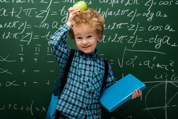 Wall Mural - happy kid holding apple and book near chalkboard with mathematical formulas