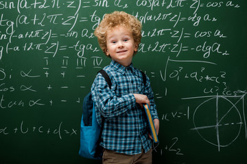 Wall Mural - happy child holding book near chalkboard with mathematical formulas