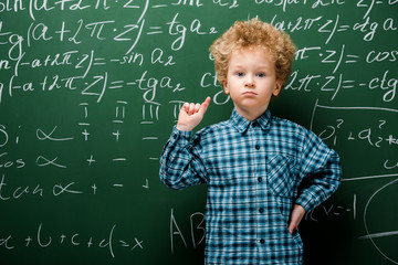 Wall Mural - smart kid standing with hand on hip near chalkboard with mathematical formulas