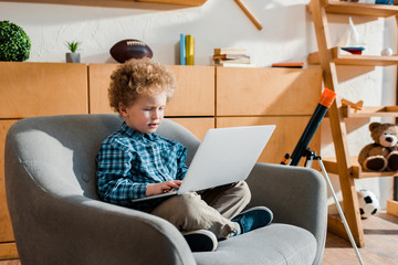 Wall Mural - cute kid sitting in armchair and using laptop