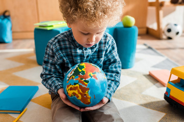 Wall Mural - smart kid looking at globe while sitting on carpet