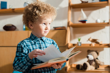 Wall Mural - curly kid holding book and looking away at home