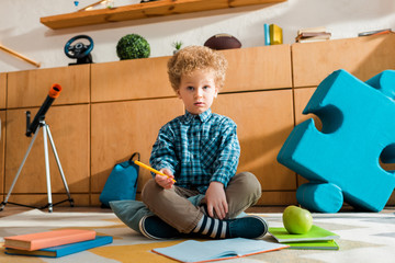 Wall Mural - curly and smart kid holding pen and sitting on floor near books