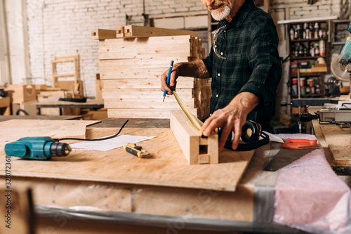 Cuadros en Lienzo Unrecognizable senior carpenter measuring length of wooden plank in workshop